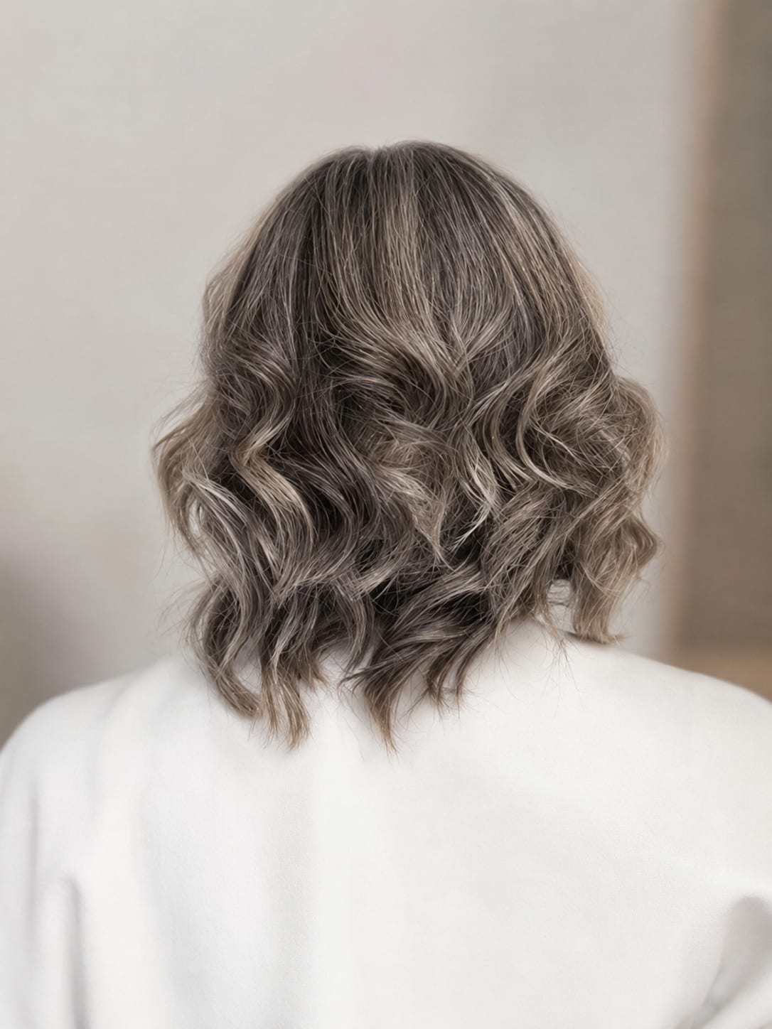 A short, softly curled grey blend — back view